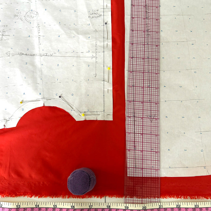 Very Vermillion fabric laid out on a table with a Hikas Gaiter pattern pinned on top and sewing notions, plastic ruler and pattern weights. 